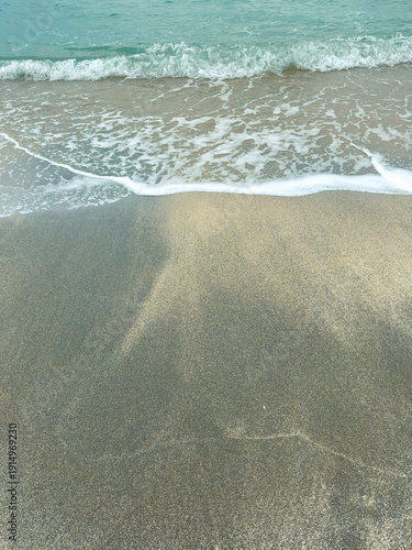 Waves rolling onto a sandy beach with light blue water during daylight hours