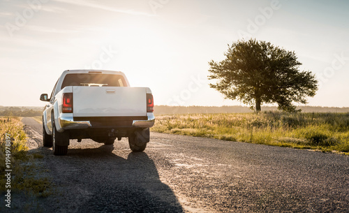 Tableau sur toile White pickup truck on a countryside paved road in late afternoon