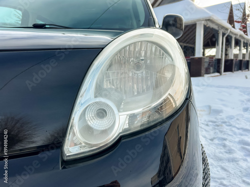 Fotografia Close view of a car headlight with snow in the background in a suburban area dur