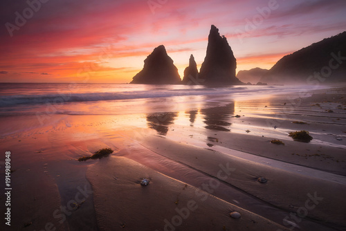 Dramatic sunset over rock formations at Praia do Rosa beach in Brazil
