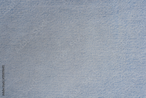 A close up full frame shot of a light blue denim fabric surface showing the detailed diagonal weave pattern of the textile material