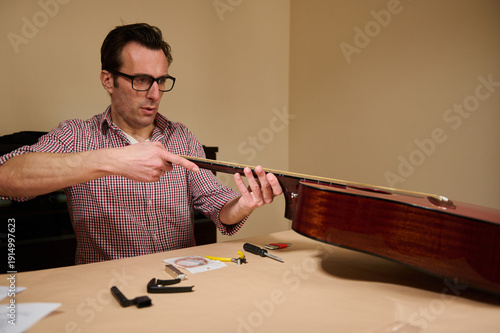 Obraz na plátně Man Adjusting Guitar Strings During Maintenance And Repair At Home Workshop