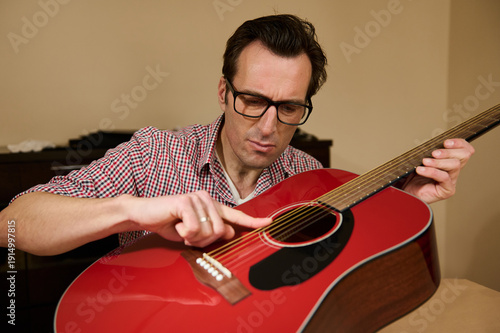 Obraz na plátně Man Adjusting Guitar Strings While Performing Maintenance and Repair on Red Acou