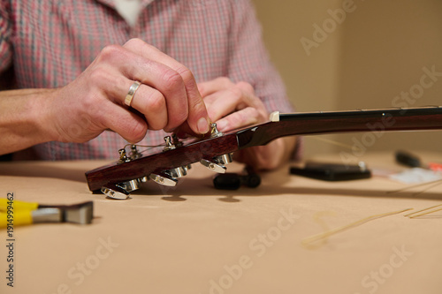 Fotografie Man Tuning Guitar Strings by Hand During Guitar Maintenance and Repair