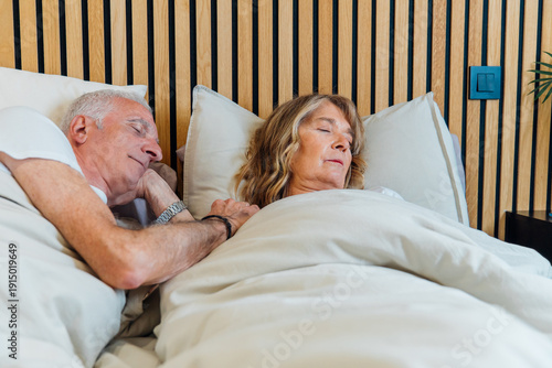 Senior couple sleeping peacefully in bed, holding hands, symbolizing love, security, and lasting companionship in their comfortable bedroom at home