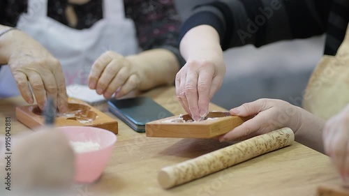 A woman's hand sprinkles flour on a wooden gingerbread mold. Close-up. Very soft focus