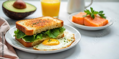 A delightful breakfast featuring a toasted sandwich layered with greens and cheese, accompanied by a fried egg, sliced salmon, avocado, and a glass of orange juice
