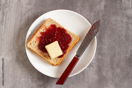 Toast with jam and butter with knife on plate, simple breakfast flat lay
