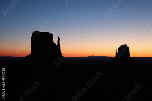 Silhouette of East and West Mitten Buttes before sunrise at Monument Valley on the Arizona–Utah border, USA. The sandstone formations stand against a gradient sky during early dawn twilight.