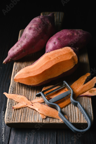 Sweet potato sliced on wooden board with peeler. Healthy cooking preparation concept
