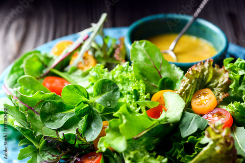 Bild auf Leinwand Mixed salad greens with cherry tomatoes and dressing on wooden table, fresh lettuce mix