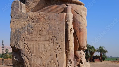 Ancient Egyptian Colossi of Memnon statues in desert landscape near Luxor, iconic archaeological landmark with tourists visiting historical pharaonic monuments