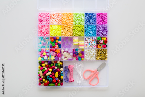 Case with colorful plastic parts, scissors, elastic strings. Light gray table background. Set for little child girl bracelet and necklaces making. Creating beaded jewellery. Flat lay. Top down view.