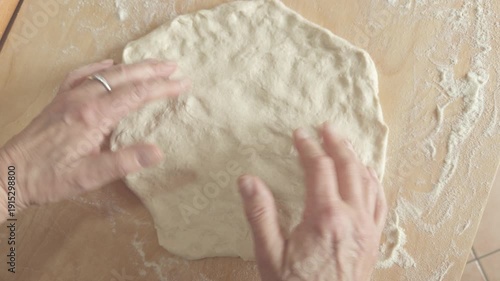 Woman hands stretching pizza dough on a wooden board, top view.