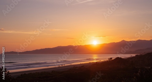 Sunset glowing over distant mountain range with tranquil beach view