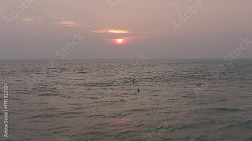 Silhouetted surfers waiting for waves at sunset on a tropical beach in Sri Lanka. Warm sunlight reflecting on the ocean surface, serene evening mood, and exotic coastal scenery. Concept of travel dest