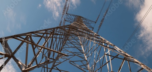 The transmission tower stretching skyward through blue clouds in dramatic low angle view