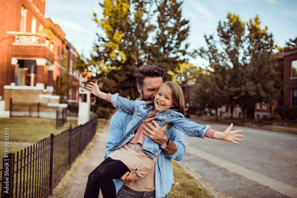 Obraz premium Father lifting happy daughter on suburban neighborhood street