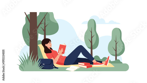 Young woman lying on a blanket under the shade of a tree and reading a book in a lush green park on a sunny day.