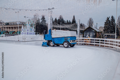 Zamboni machine prepares ice rink at winter park in the evening with Christmas lights and decorations