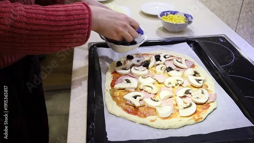 young woman preparing homemade pizza by placing ingredients on fresh dough