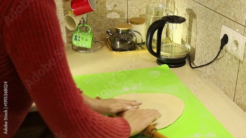 Young woman preparing homemade pizza, rolling out fresh dough on a kitchen table.