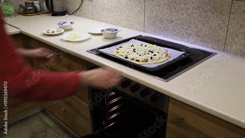 Young woman carefully placing a baking tray with homemade pizza into the oven. 