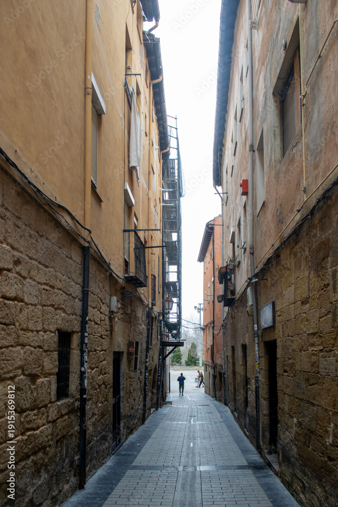 Obraz premium Persona caminando por una calle estrecha y antigua con fachadas de piedra y colores cálidos en Logroño, España