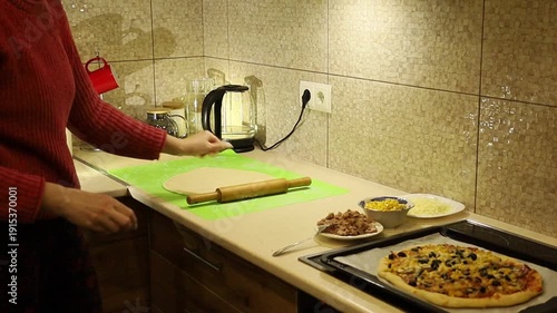Young woman preparing homemade pizza, rolling out fresh dough on a kitchen table.