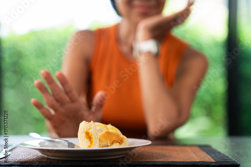 Healthy senior woman making a mindful food choice by refusing pastry in a bright natural setting. Promotes self-awareness, healthy aging, and intentional eating habits for a balanced lifestyle