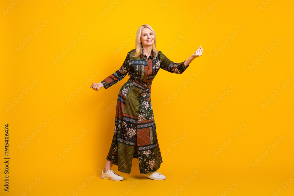 Obraz premium Elegant mature woman wearing a patchwork dress smiles and poses against a vibrant yellow background for a stylish casual fashion image
