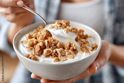 A close-up shot capturing a person holding a bowl of yogurt with granola, showcasing a spoonful of the delicious mixture, focusing on healthy eating and nutrition.