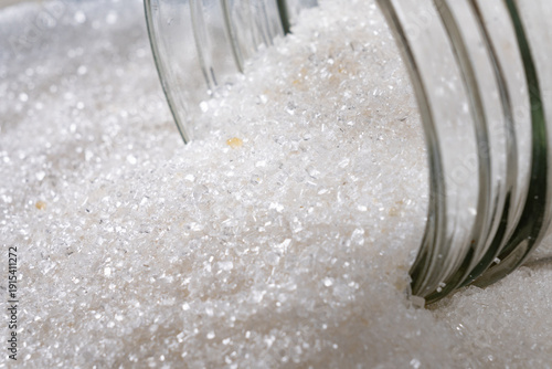 Tableau sur toile White sugar spilling from a glass jar onto a light marble surface