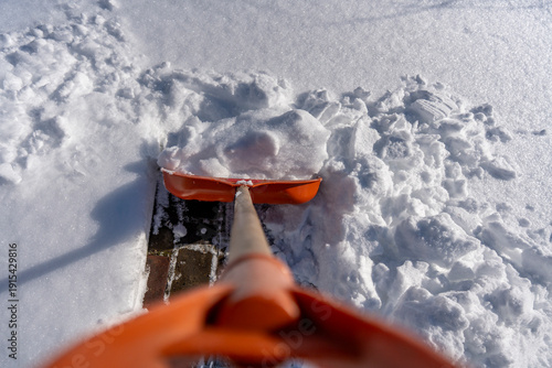 Point of view of snow removal with an orange shovel clearing fresh snow from a walkway on a sunny winter day outdoor seasonal maintenance concept, closeup