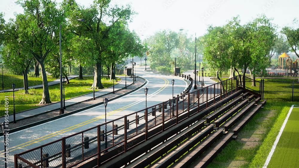 Fototapeta premium A peaceful scene showcases a winding road bordered by vibrant trees. Sunlight dances through the leaves, creating a serene atmosphere, while distant playground equipment adds charm.