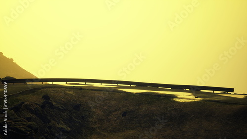 Bilde på lerret A winding road disappears into the hazy horizon as the sun sets, casting a soft yellow glow over the landscape