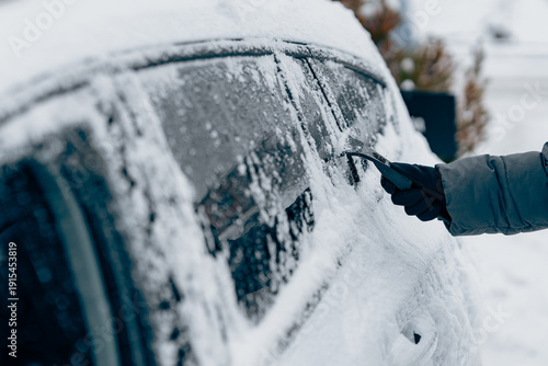 Scraping ice and snow from car windshield with plastic scraper on a cold winter day