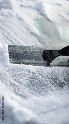 Scraping ice and snow from car windshield with plastic scraper on a cold winter day
