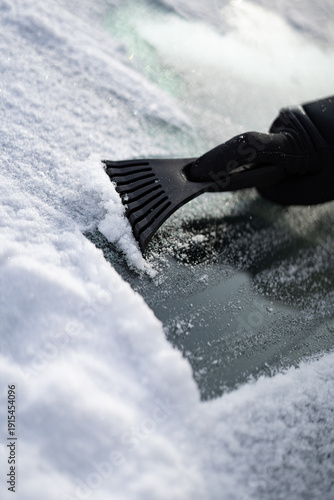 Scraping ice and snow from car windshield with plastic scraper on a cold winter day