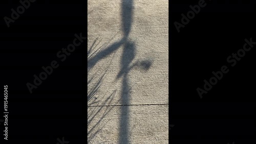 Shadow of caution tape wavers by edge of grass in a somewhat fitful breeze along a concrete sidewalk on a sunny afternoon. Motifs of public safety, awareness, and risk avoidance. Vertical B-roll, 4K.