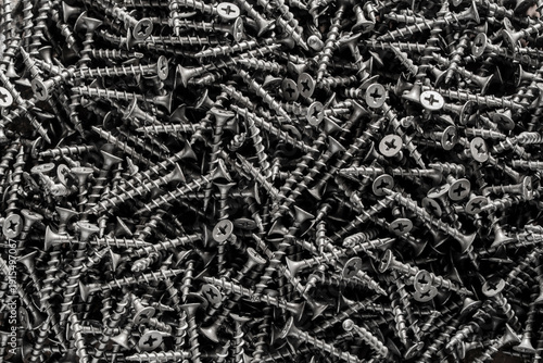Many black metal self tapping screws for construction work, closeup, top view. New metal fasteners self tapping screws for connecting wooden elements. Background and texture of metal screws