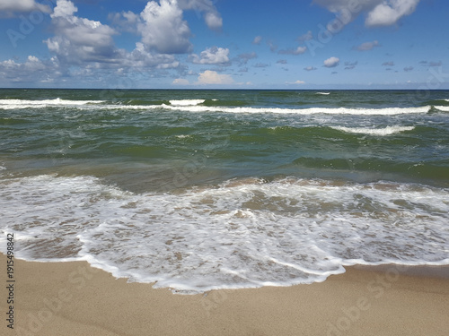 Sandy beach with turquoise waves and white foam under blue sky