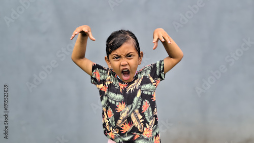 Foto Cute Asian child is making a playful, roaring gesture with both hands raised on grey background isolated