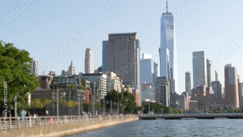 New York City Manhattan downtown financial district skyline, United States. Urban waterfront cityscape, World Trade Center skyscraper building, Hudson River Park, people walk on riverfront promenade.