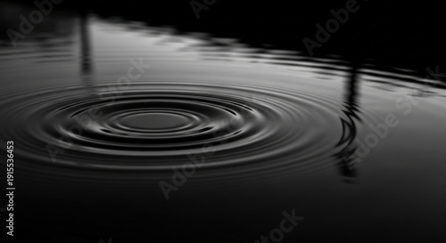 Concentric water ripples spread on a reflective surface in a dark monochrome close-up against a pure black background.