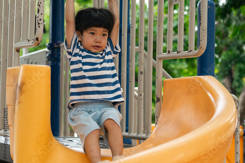 A portrait of a cute and cheerful little Asian boy as he plays on an outdoor playground. The kid is laughing heartily as they enjoy the Slide in a public park, a genuine moment of happy childhood.