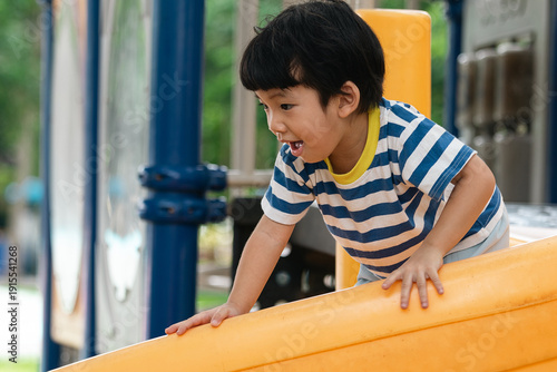 A portrait of a cute and cheerful little Asian boy as he plays on an outdoor playground. The kid is laughing heartily as they enjoy the Slide in a public park, a genuine moment of happy childhood.
