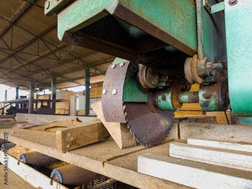 Professional wood sawing machine with protective guard in an industrial factory.