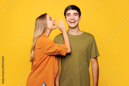 Obraz na plátně Young couple two friends family man woman wear casual clothes whisper gossip tell secret behind her hand sharing news together isolated on pastel plain light yellow color background studio portrait