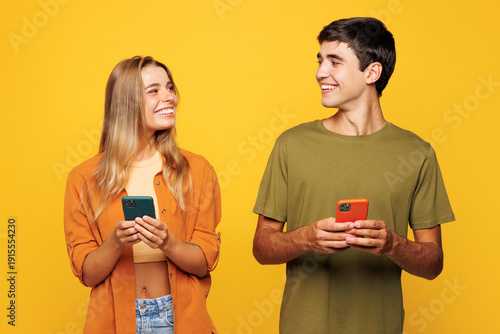 Foto Young happy couple friends family man woman wear casual clothes hold in hand use mobile cell phone together look to each other isolated on pastel plain light yellow color background studio portrait